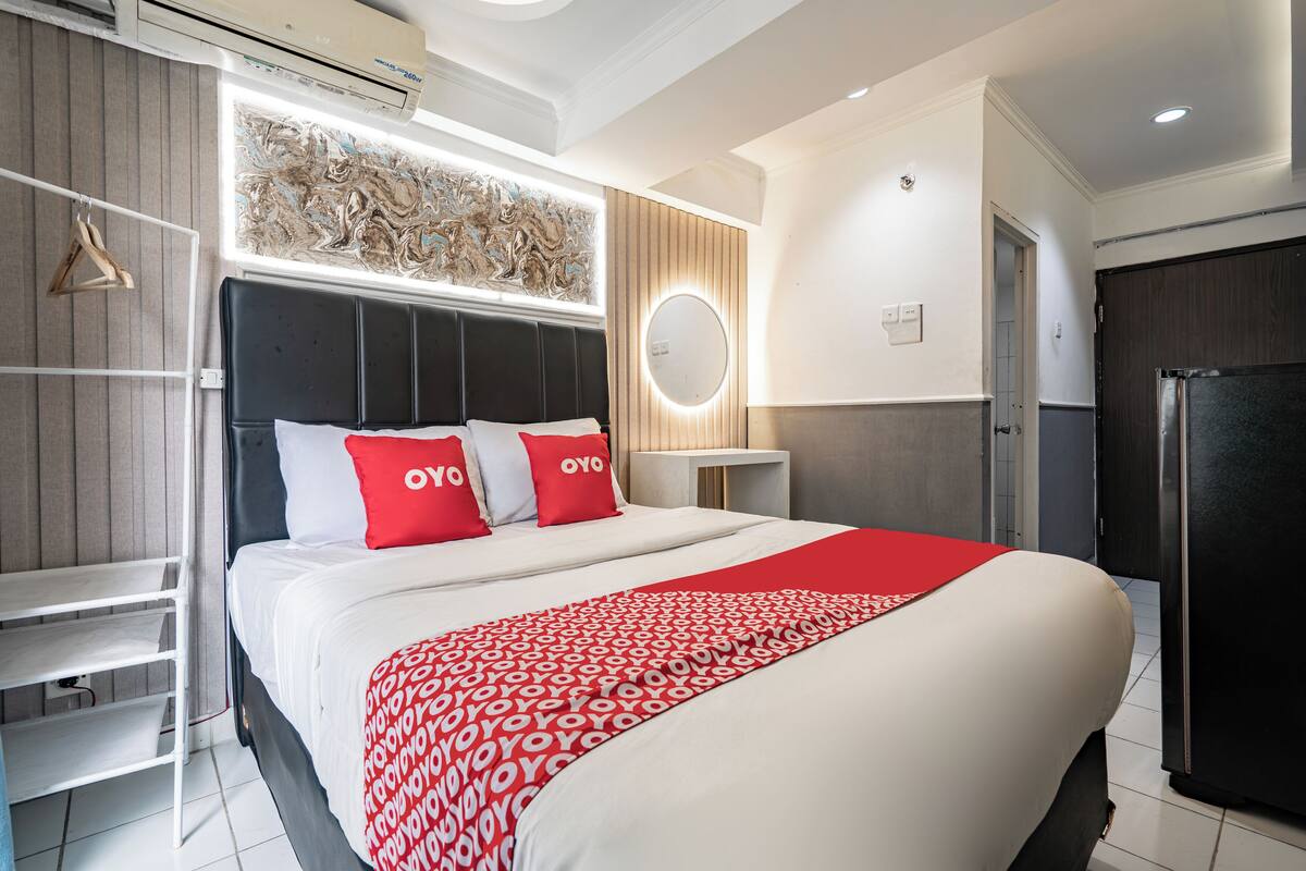 A modern hotel room with a large bed, a wardrobe, a bedside table, and a wall-mounted air conditioning unit.