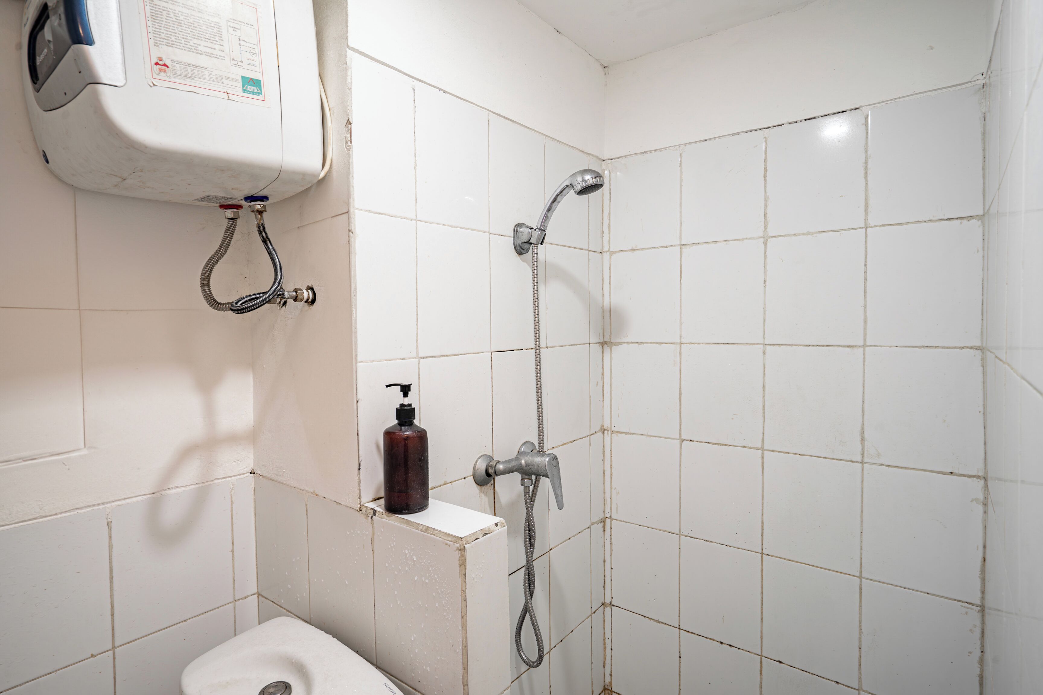 Une petite salle de bain comprenant des toilettes, une douche et un distributeur de savon fixé au mur.
