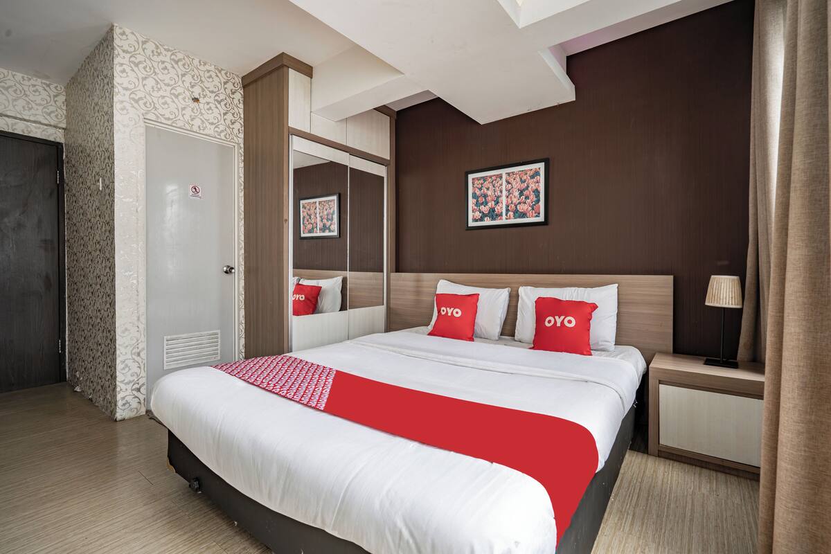 A hotel room with a large bed, a nightstand, a mirror, and a door.