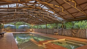 An indoor swimming pool with a covered roof, tiled flooring, and a view of greenery outside. - StayAU 1BR Rustic Picturesque Cottage (Badger Creek)