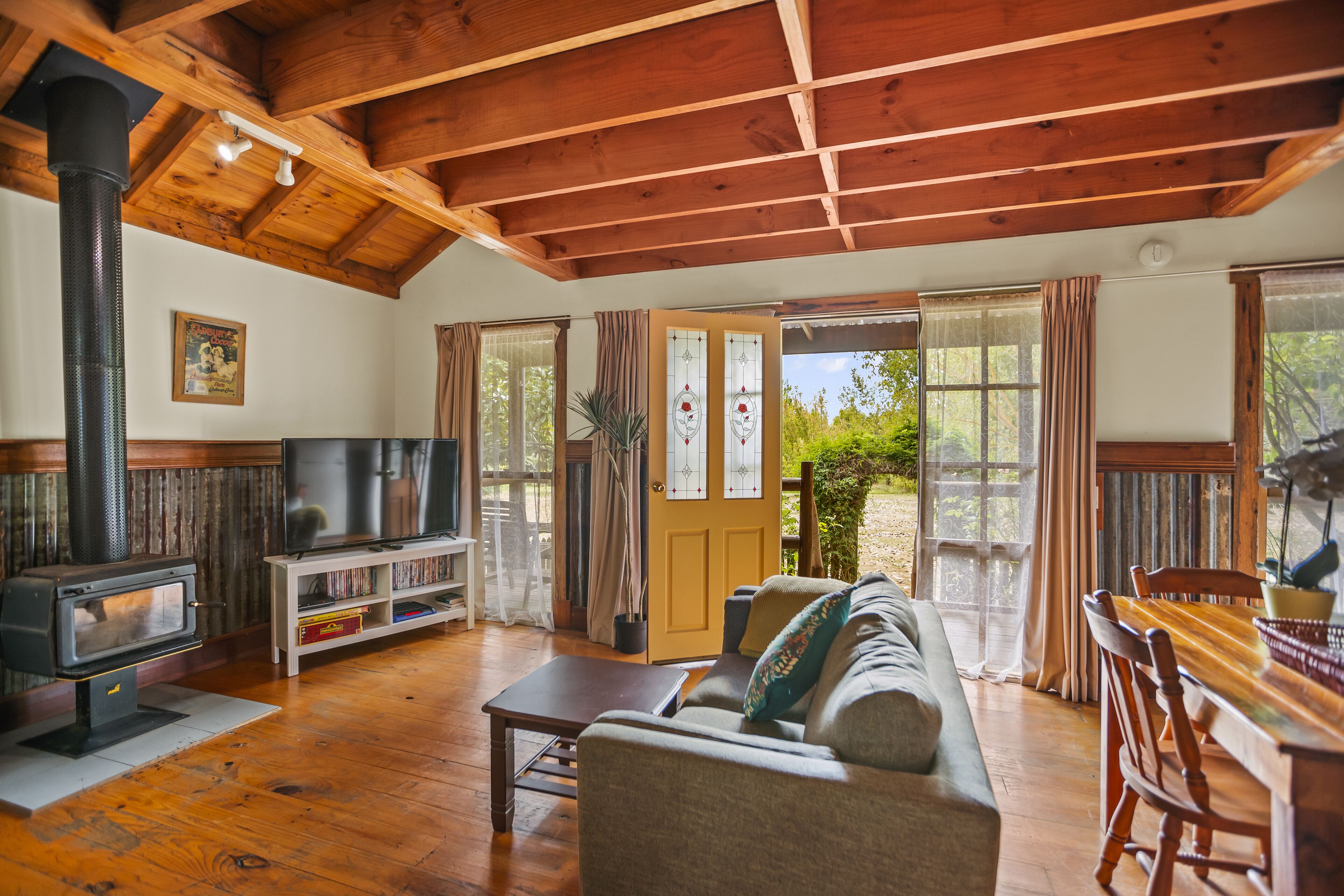 A cozy living room with a wooden ceiling, a fireplace, a television, a sofa, and a dining table.