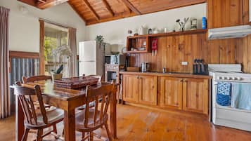 A wooden kitchen with a dining table, chairs, a refrigerator, a microwave, and a stove.