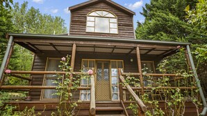 A wooden cabin with a porch, a front door, and a window. - StayAU 1BR Rustic Picturesque Cottage (Badger Creek)