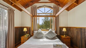 A bedroom with a wooden ceiling, a large window, a bed with white bedding, two bedside tables with lamps, and a 'Stay' pillow. - StayAU 1BR Rustic Picturesque Cottage (Badger Creek)