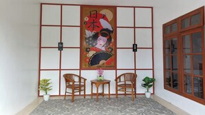 A traditional Japanese room with tatami flooring, a shoji screen, and a large poster of a geisha. There are two wooden chairs and a small table with a vase of flowers. - Hotel O Ipeda Family Residence (Banyuwangi)