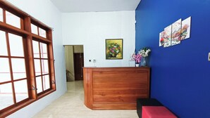 A reception area with a wooden desk, a blue wall with artwork, and a large window with a view. - Hotel O Ipeda Family Residence (Banyuwangi)