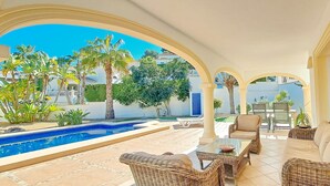 A covered outdoor area with a swimming pool, wicker furniture, and a view of the surrounding buildings. - Villa Sollero by Solidays - Moraira, Costa Blanca (Moraira)