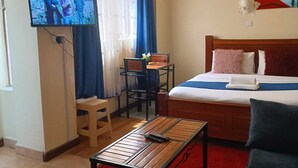 Habitación de hotel con cama, televisión montada en la pared, una mesita, una silla y alfombra roja.