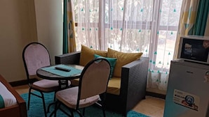 Una habitación pequeña y acogedora con un sofá, dos sillones, una mesa y un refrigerador.