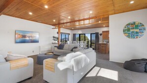 A modern living room with a large sofa, a coffee table, and a dining area with chairs. There is a kitchen area with wooden cabinets and a large window. - Panoramic mountain and rural views - central to key destinations
 (Te Awamutu)