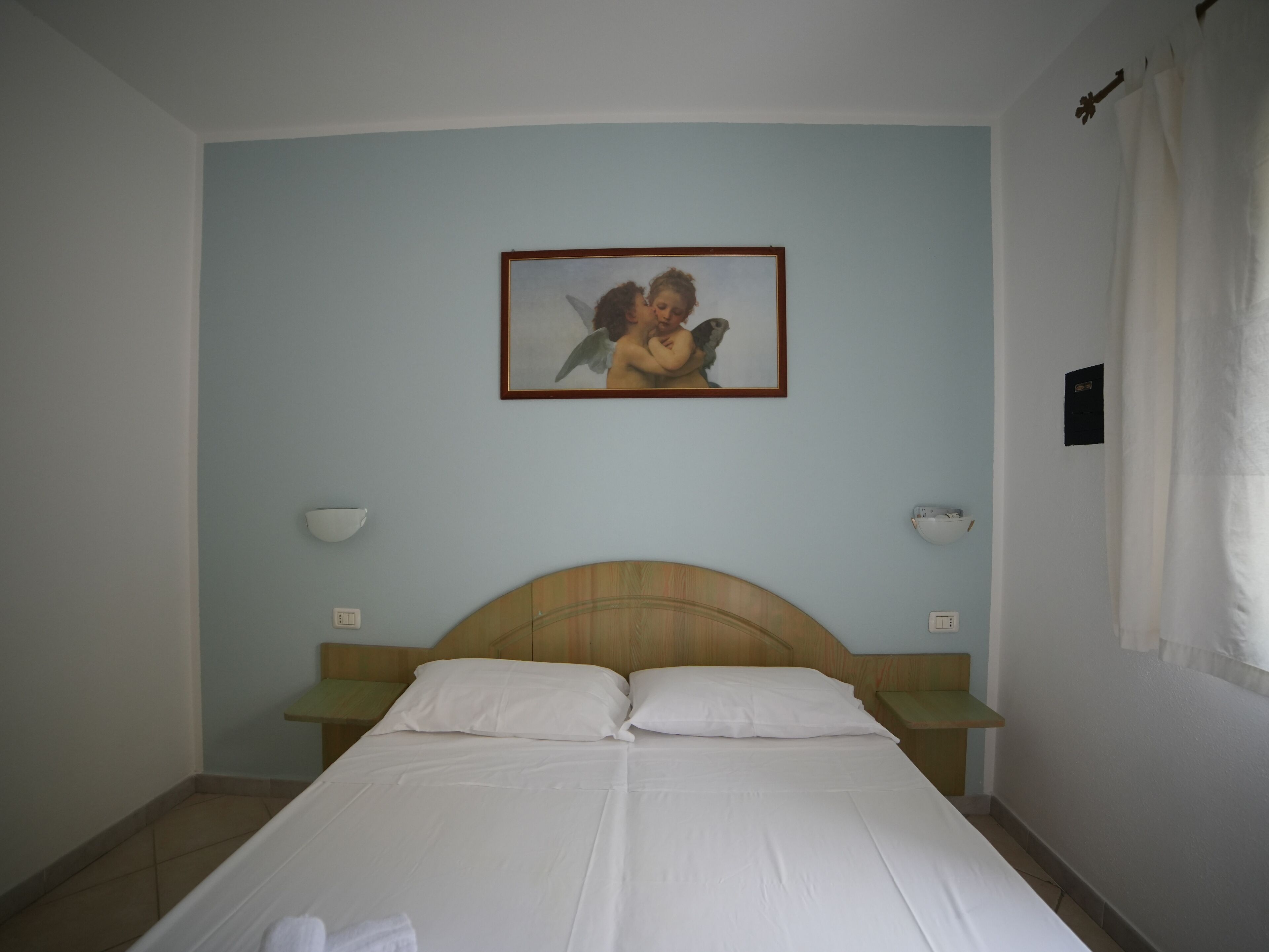 A bedroom with a bed, two bedside tables, a nightstand, a wall-mounted lamp, and a framed picture.