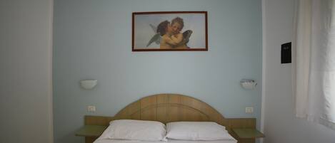 A bedroom with a bed, two bedside tables, a nightstand, a wall-mounted lamp, and a framed picture.