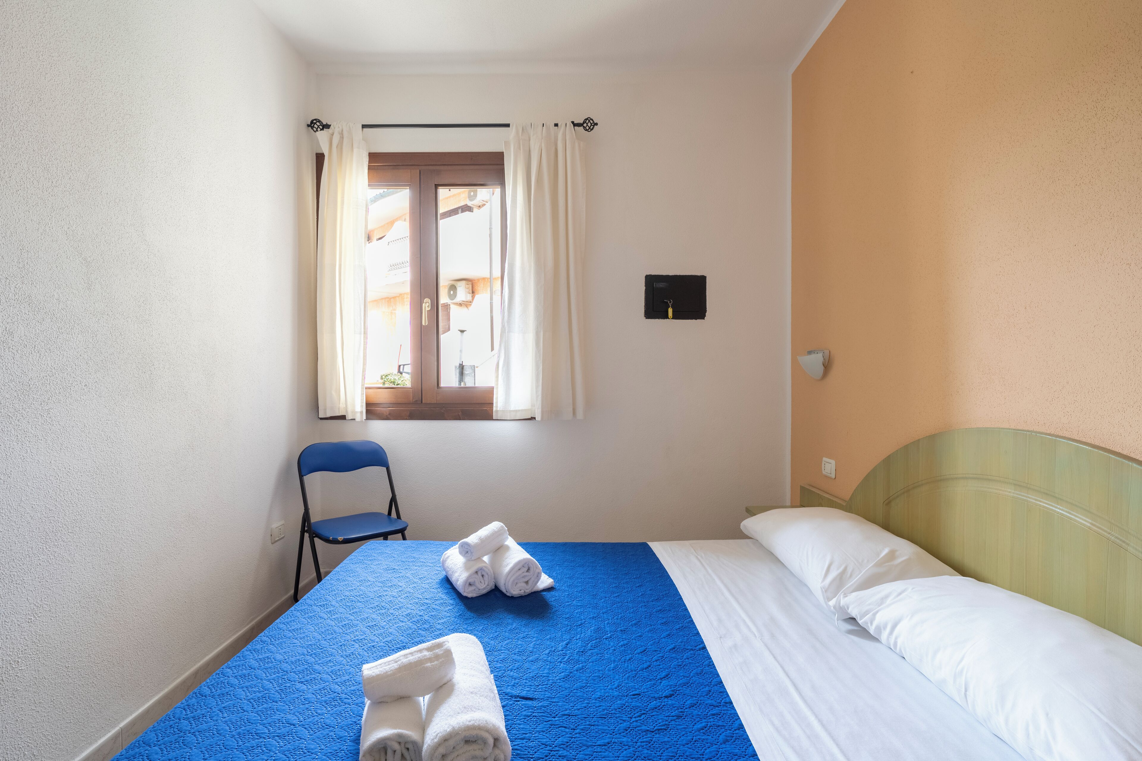 A hotel room with a bed, a chair, and a window with curtains.