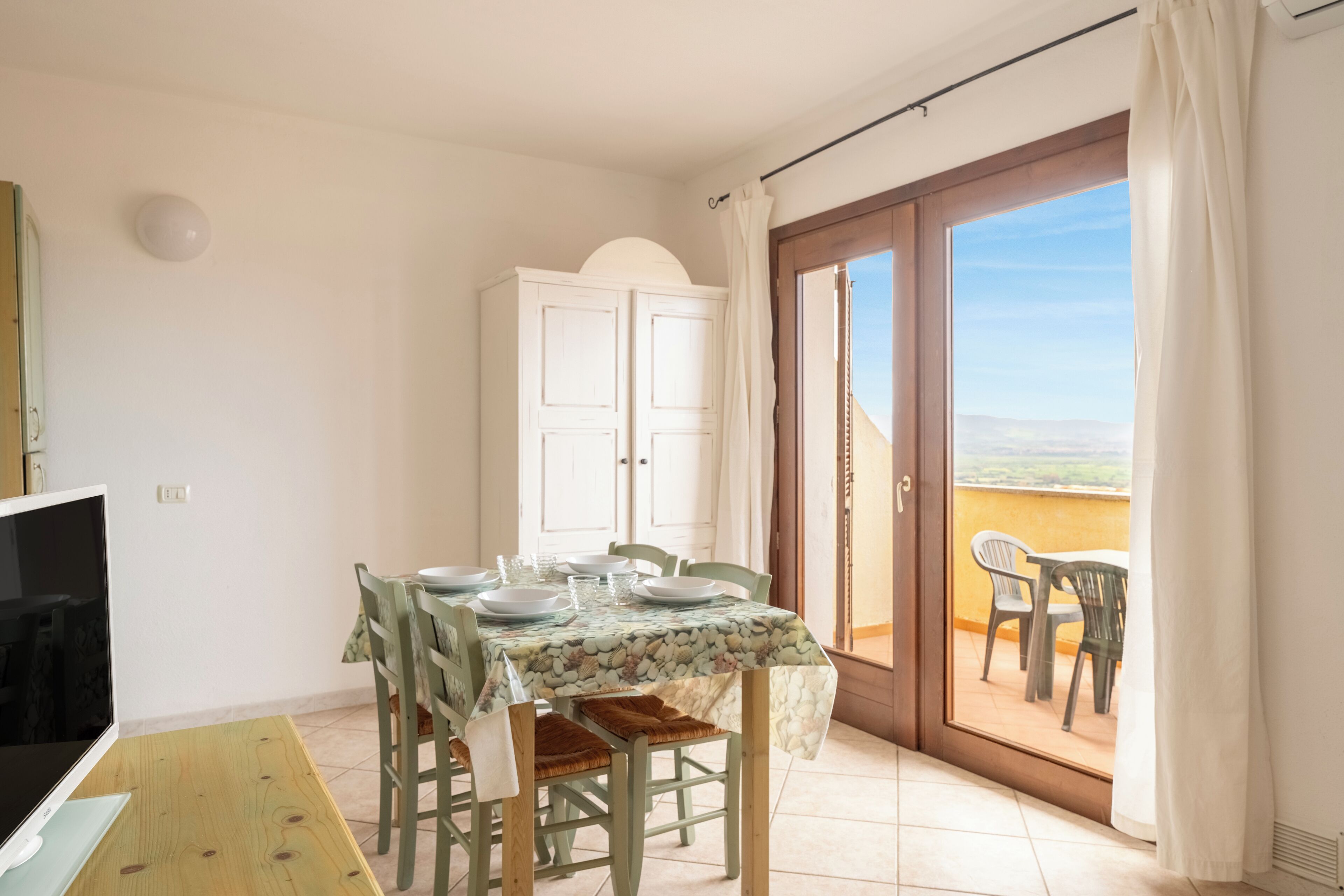 A dining area with a table set for four, a cabinet, and a balcony with chairs.
