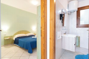 Een slaapkamer met een bed, nachtkastje en een badkamer met wastafel en spiegel.