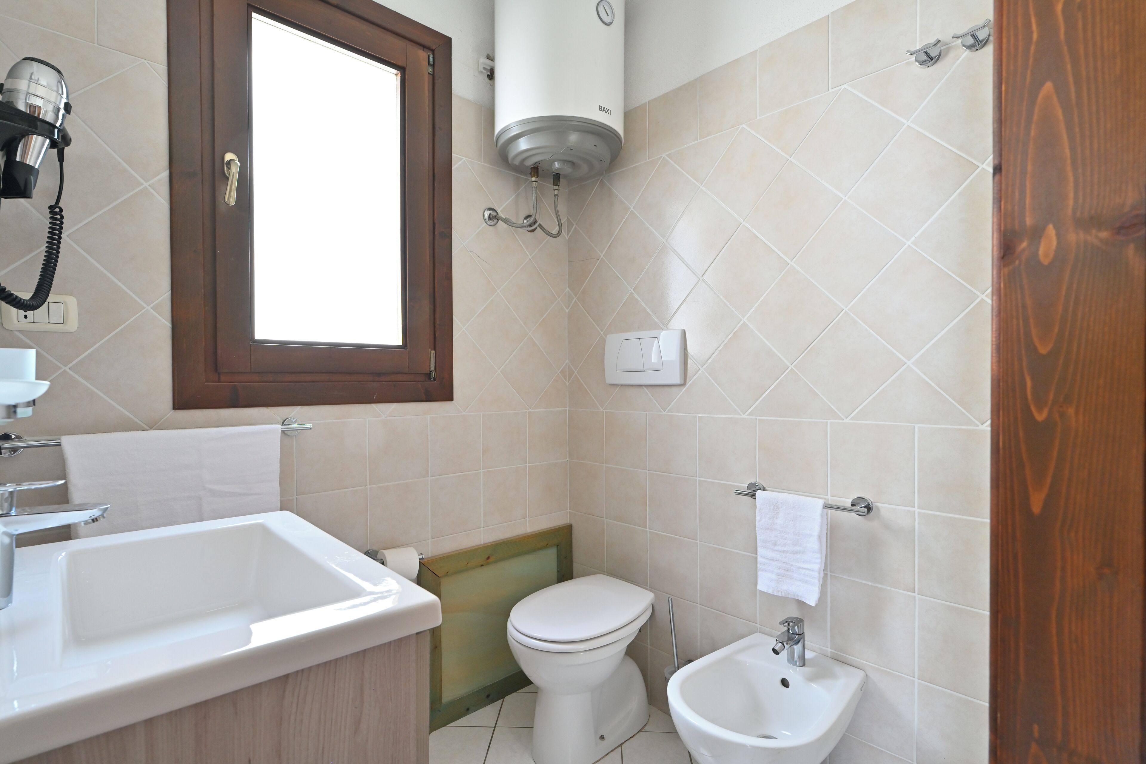 Un baño con lavamanos, inodoro, bidé y un secador de pelo montado en la pared.