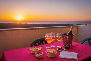 Une table dressée pour un repas avec vue sur le coucher de soleil, comprenant une bouteille de champagne, des verres et des amuse-gueules.