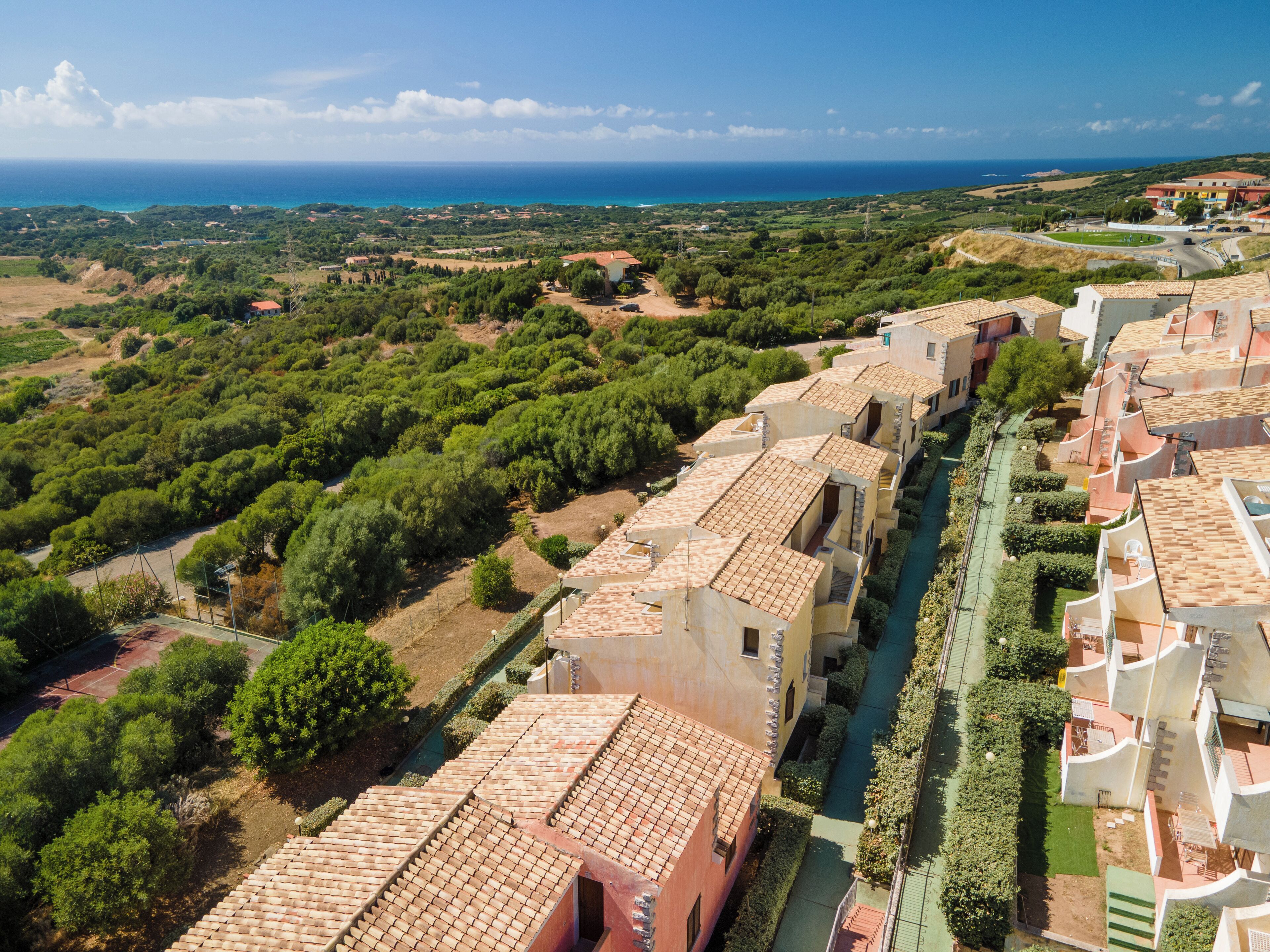 Un área residencial costera con edificios de tejados de terracota, espacios verdes y vistas al mar.