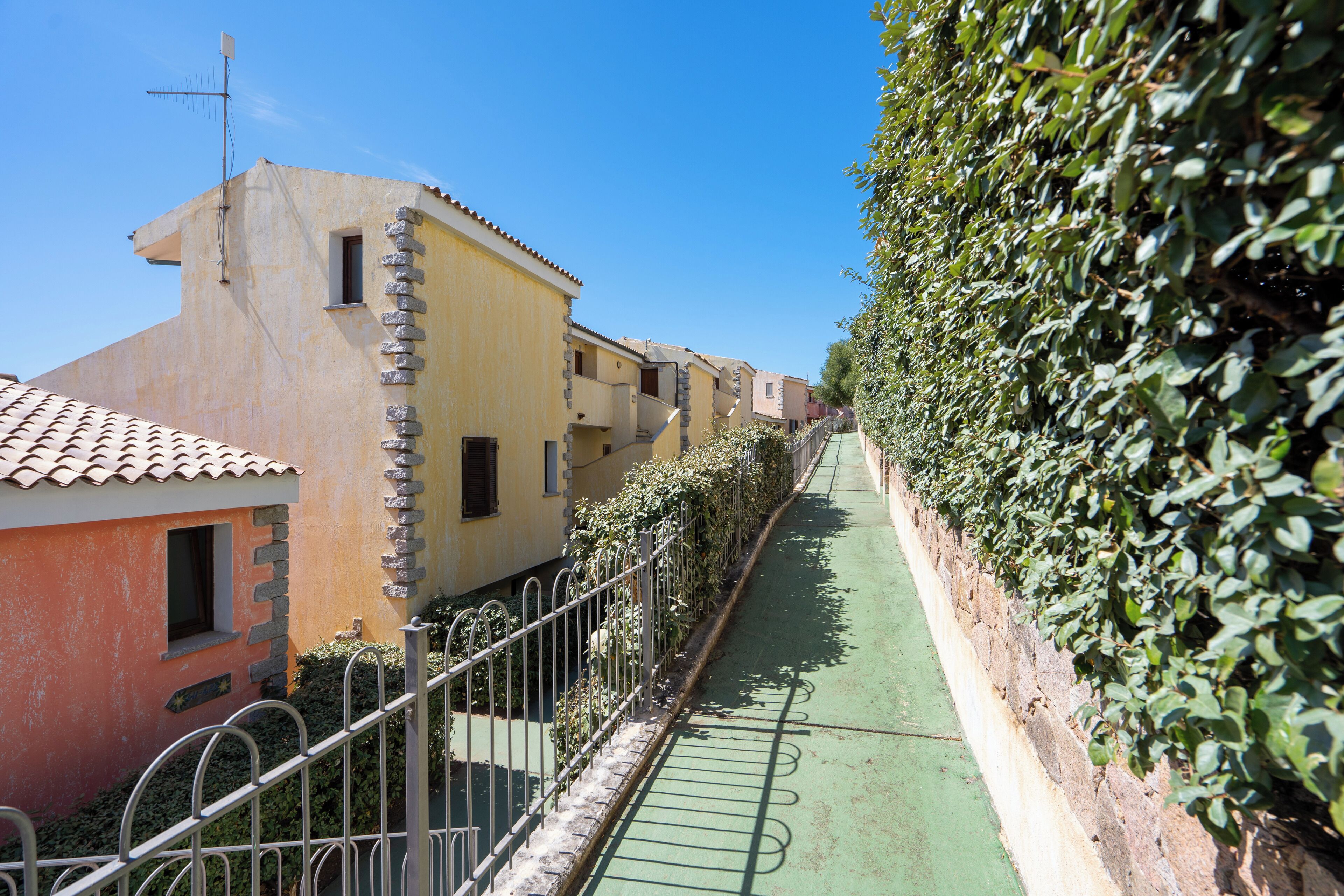 A narrow alley with buildings on either side, a green bike lane, and a metal fence.