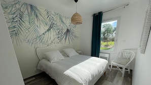 Ein Schlafzimmer mit einem Bett, einem Sessel, einem Fenster und einer Wand mit Blätermotiv.