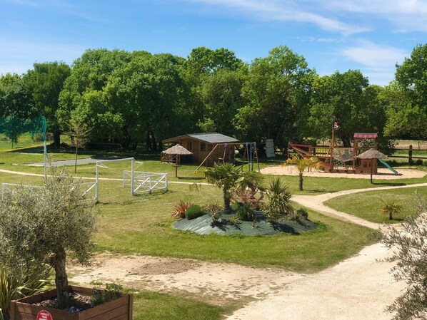 A park with a wooden playhouse, a soccer goal, and a small building with a red roof.