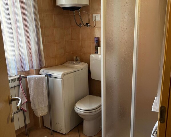 A compact bathroom with a washing machine, toilet, and a shower area.