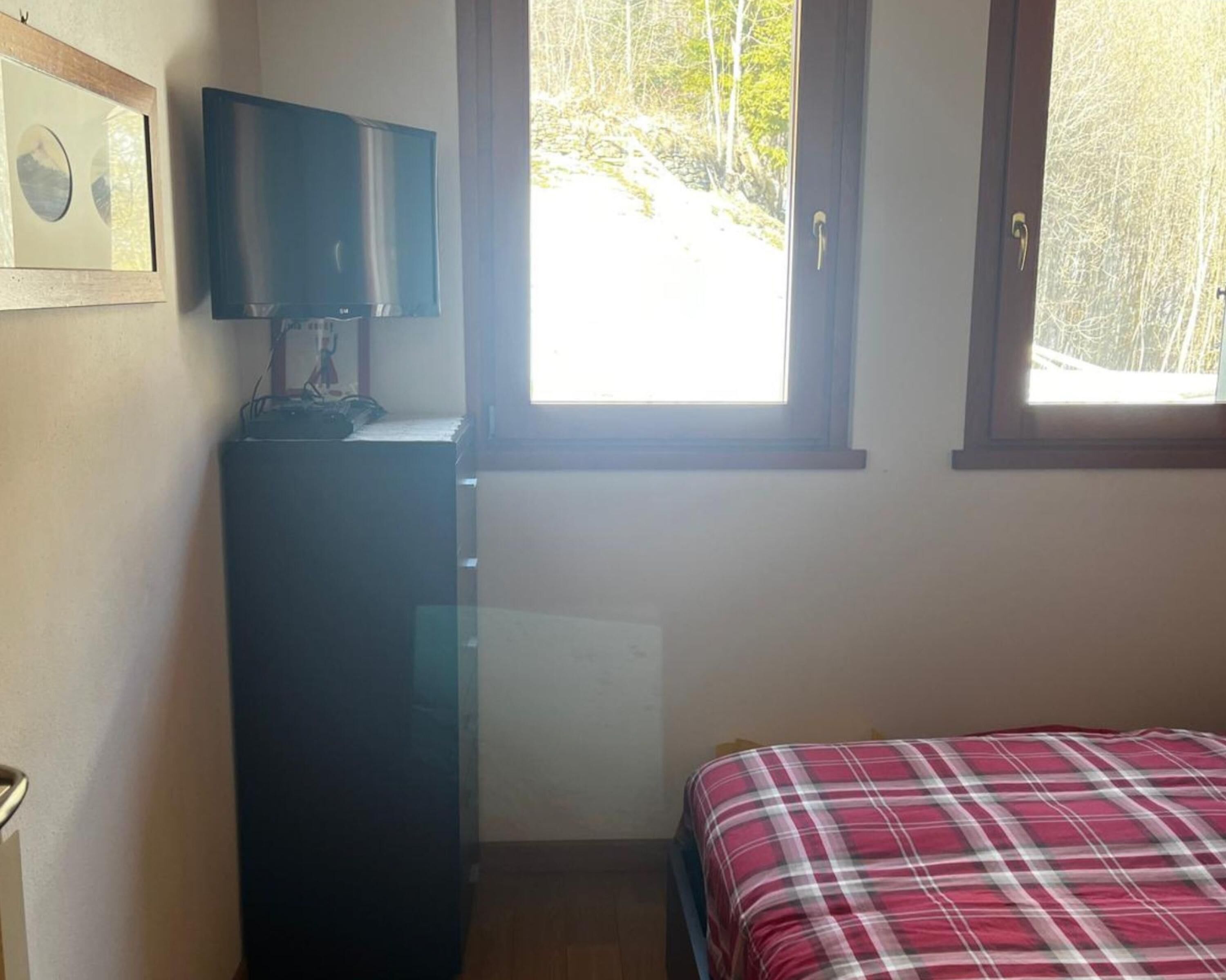A bedroom with a bed, a dresser, a television, and a window with a view of trees.