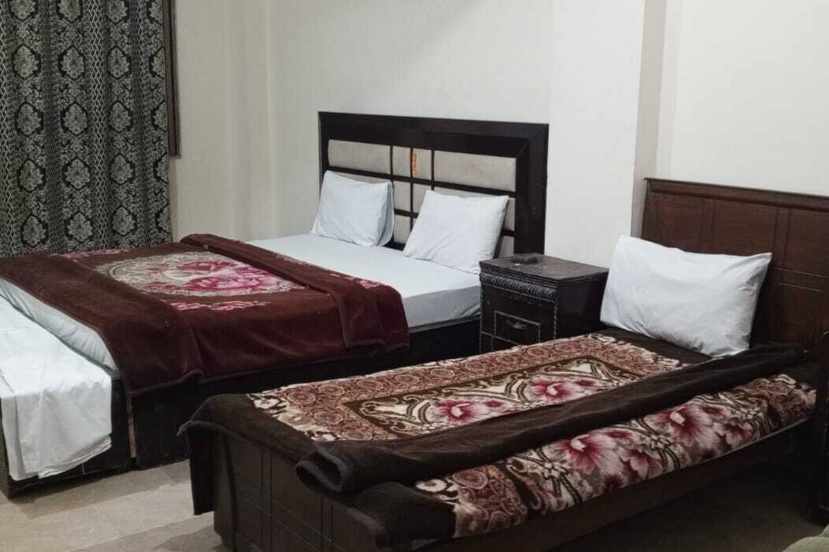 Een kamer met twee bedden, een nachtkastje, een kast en een kamerbreed tapijt met een patroon.