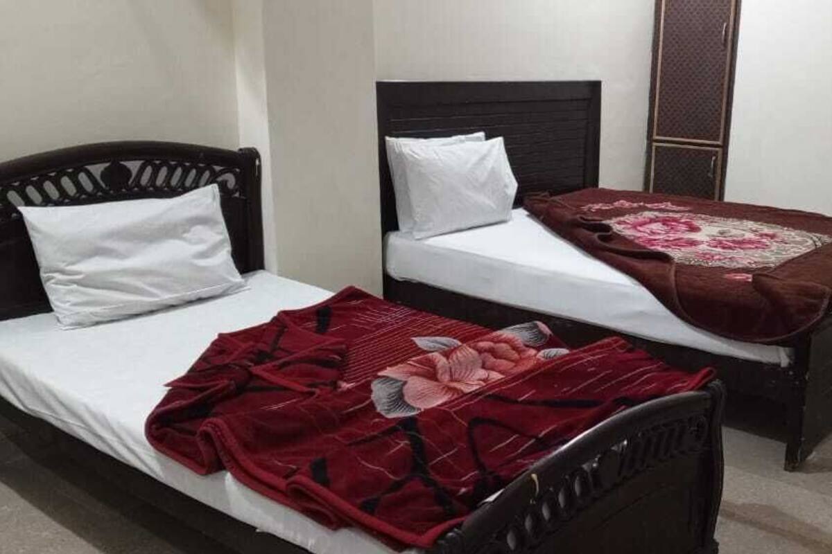 Een kamer met twee éénpersoonsbedden, elk met hoofdbord en een wit matras. Op het een bed ligt een rode deken, op het andere een bruine.