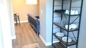 A living room with a sofa, a coffee table, and a bookshelf filled with white dishes and glasses. - Desert Casita Guesthouse (Joshua Tree)