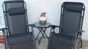Two black mesh chairs with metal frames and a small table with a 'WELCOME' sign and a gnome decoration. - Desert Casita Guesthouse (Joshua Tree)