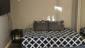 A bedroom with a bed, two pillows, a nightstand, and a TV mounted on the wall. - Desert Casita Guesthouse (Joshua Tree)