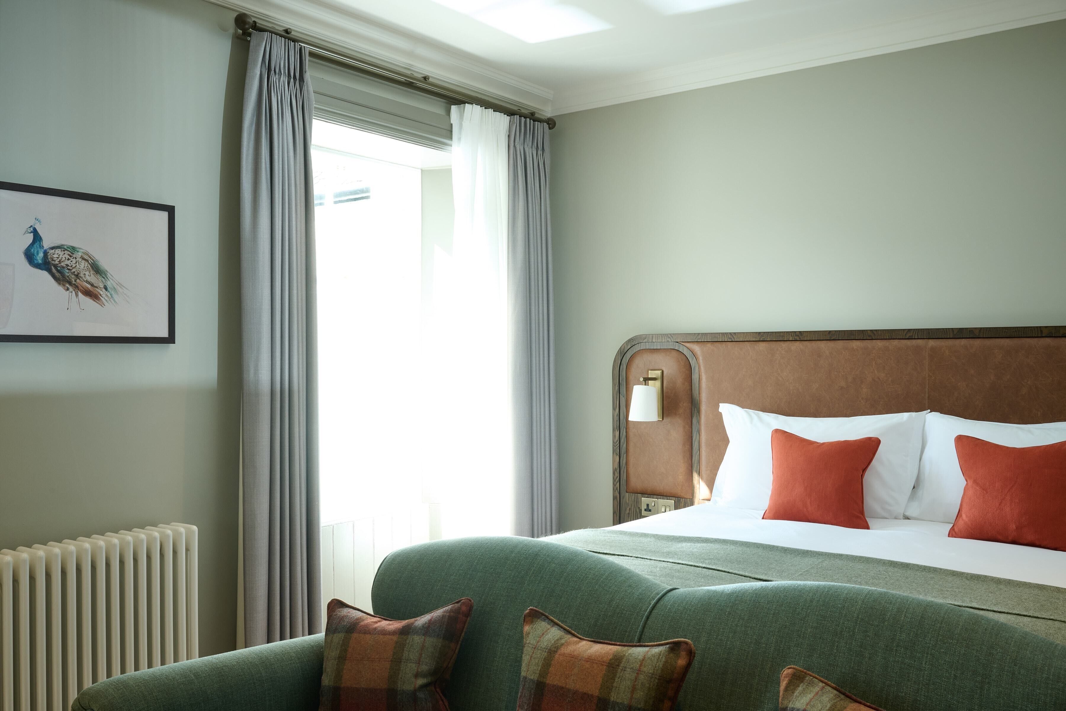 Una habitación de hotel con una cama grande, un sofá verde y un cuadro de un pavo real en la pared.