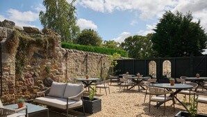Une terrasse extérieure avec des murs en pierre, des meubles en osier et des plantes en pot.