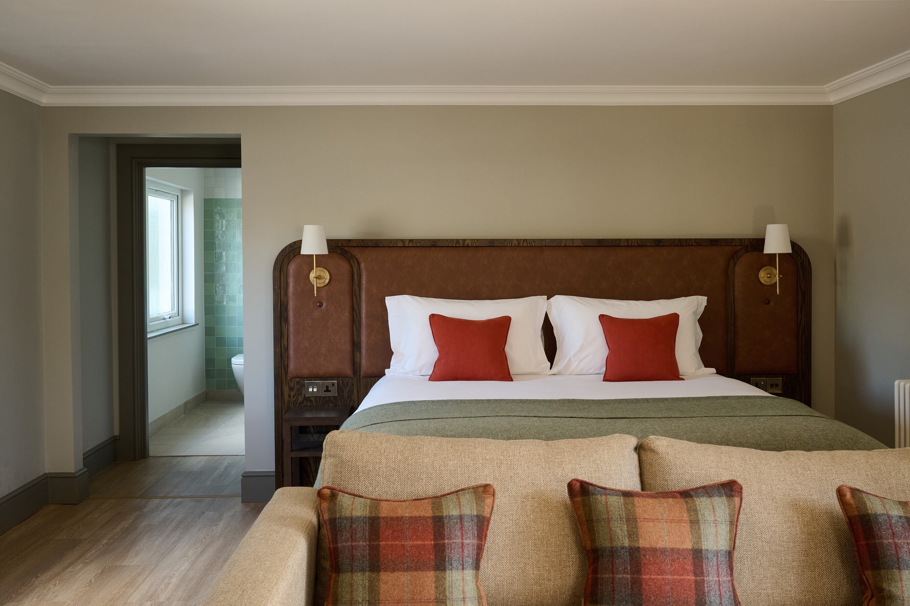 Une chambre d’hôtel avec un grand lit, deux tables de chevet, une commode, une fenêtre et une porte donnant sur une salle de bain.