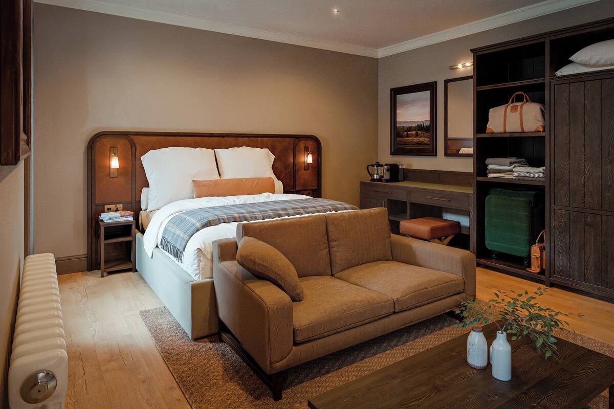 Um quarto com cama, sofá, guarda-roupa de madeira e uma mesinha com vasos.