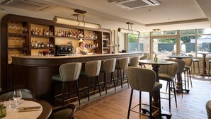 Un espace bar avec un barman, des tabourets de bar et une variété de bouteilles et de verres exposés sur des étagères.