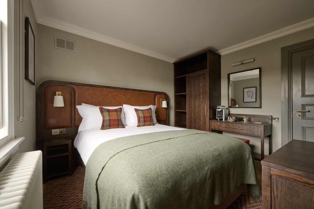 Quarto de hotel com uma cama grande, mesa de cabeceira, cômoda, espelho e radiador.
