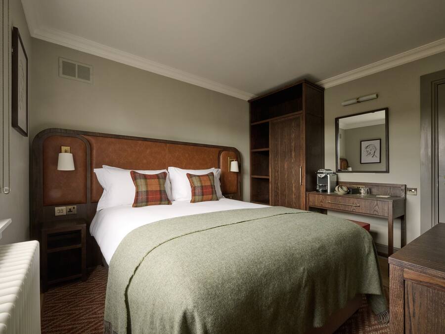 Quarto de hotel com uma cama grande, mesa de cabeceira, cômoda, espelho e radiador.
