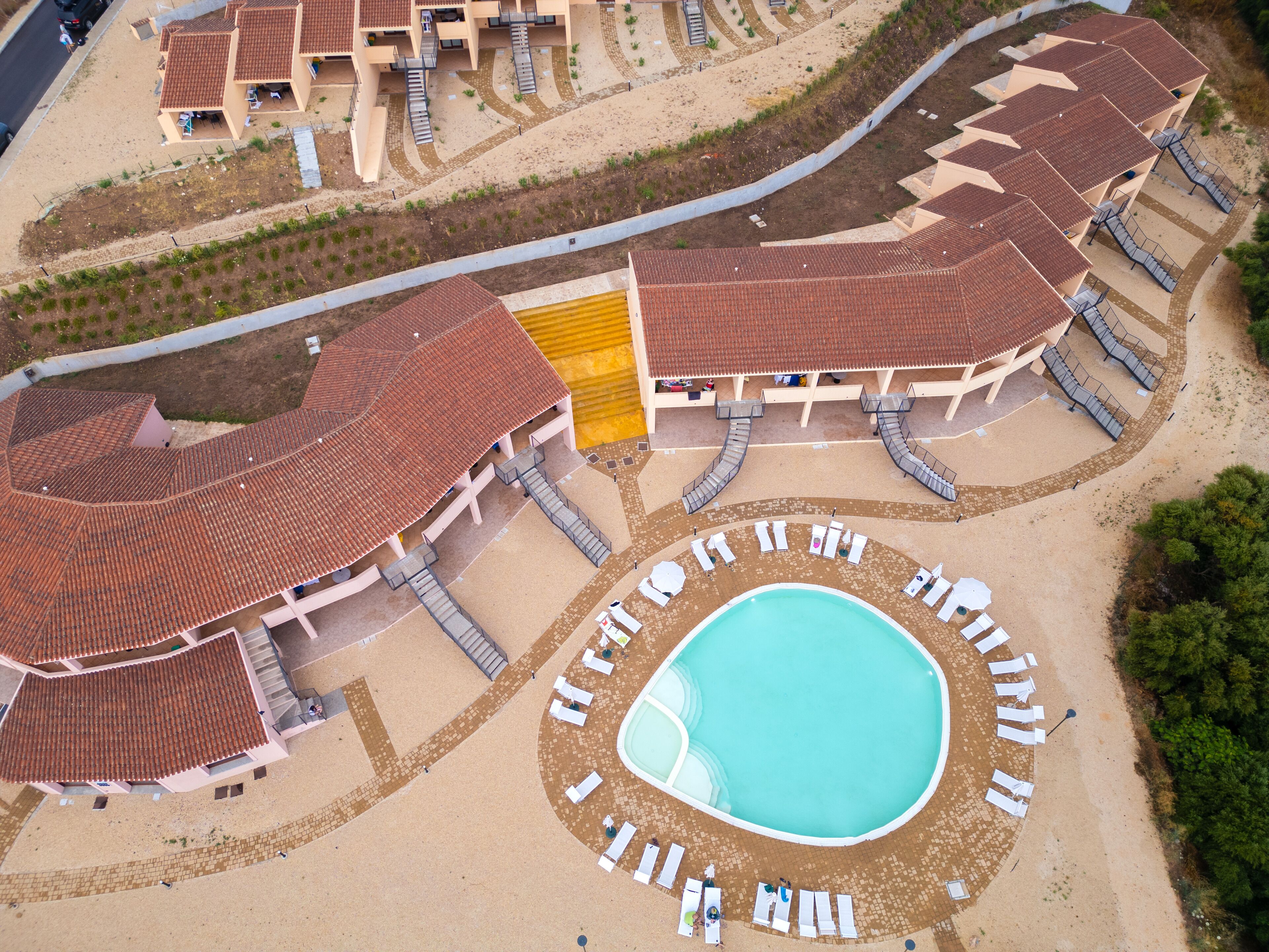 An aerial view of a resort with a central swimming pool, multiple lounge areas, and a variety of building structures.