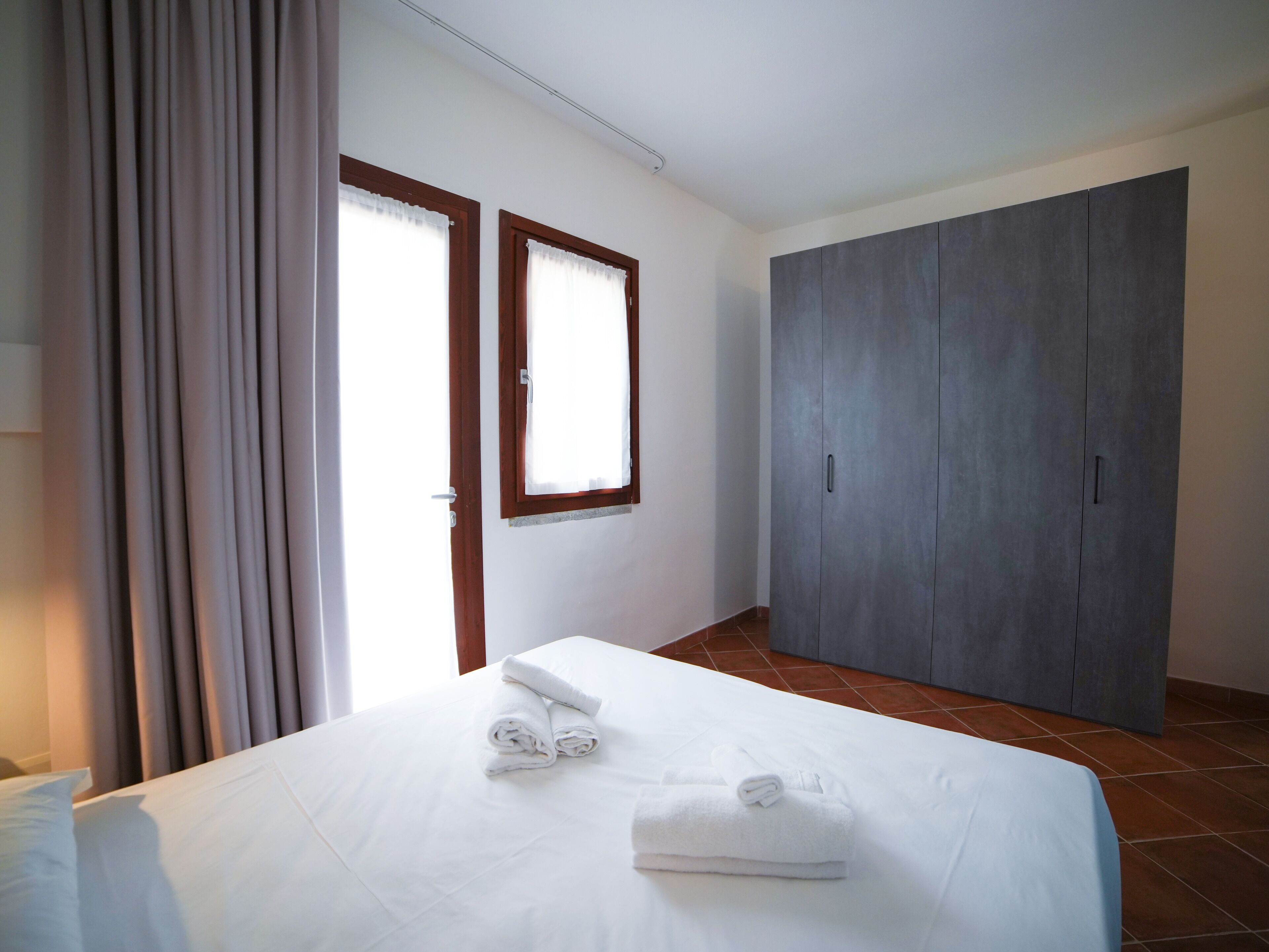 A bedroom with a bed, two windows, a wardrobe, and a curtain.
