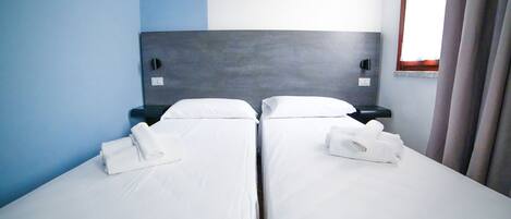 Habitación de hotel con dos camas individuales, cada una con una toalla blanca doblada con cuidado.