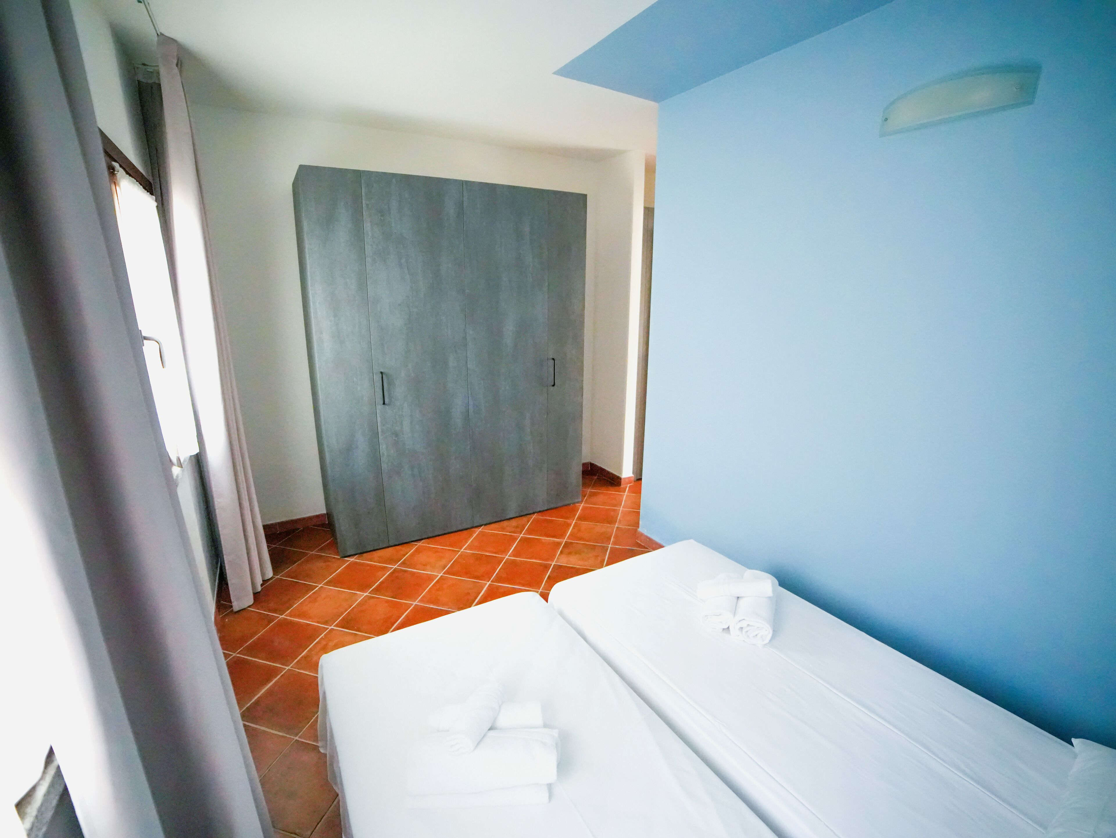 Ein Hotelzimmer mit zwei Betten, einem grauen Wandschrank und einer blauen Wand.