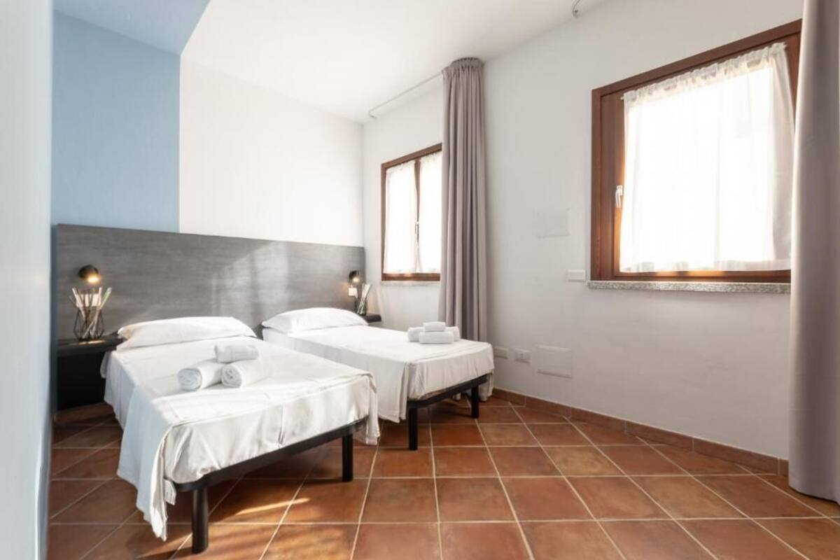 A hotel room with two beds, a large window with curtains, and a tiled floor.