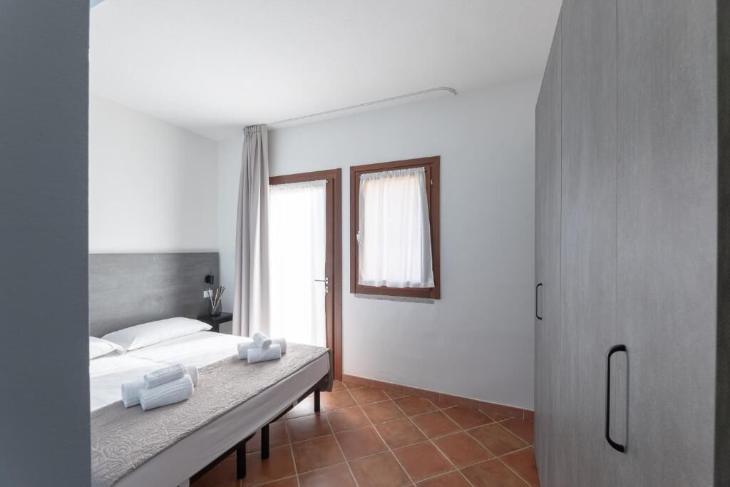 Un dormitorio con una cama, dos ventanas con cortinas, una puerta y una lámpara fijada a la pared.