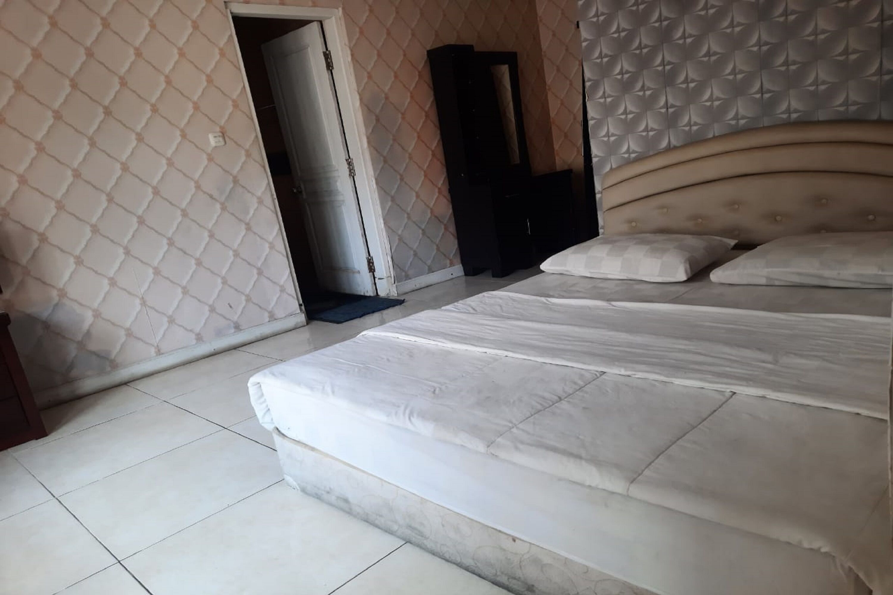 Quarto com cama, guarda-roupa e porta que dá para outro espaço.
