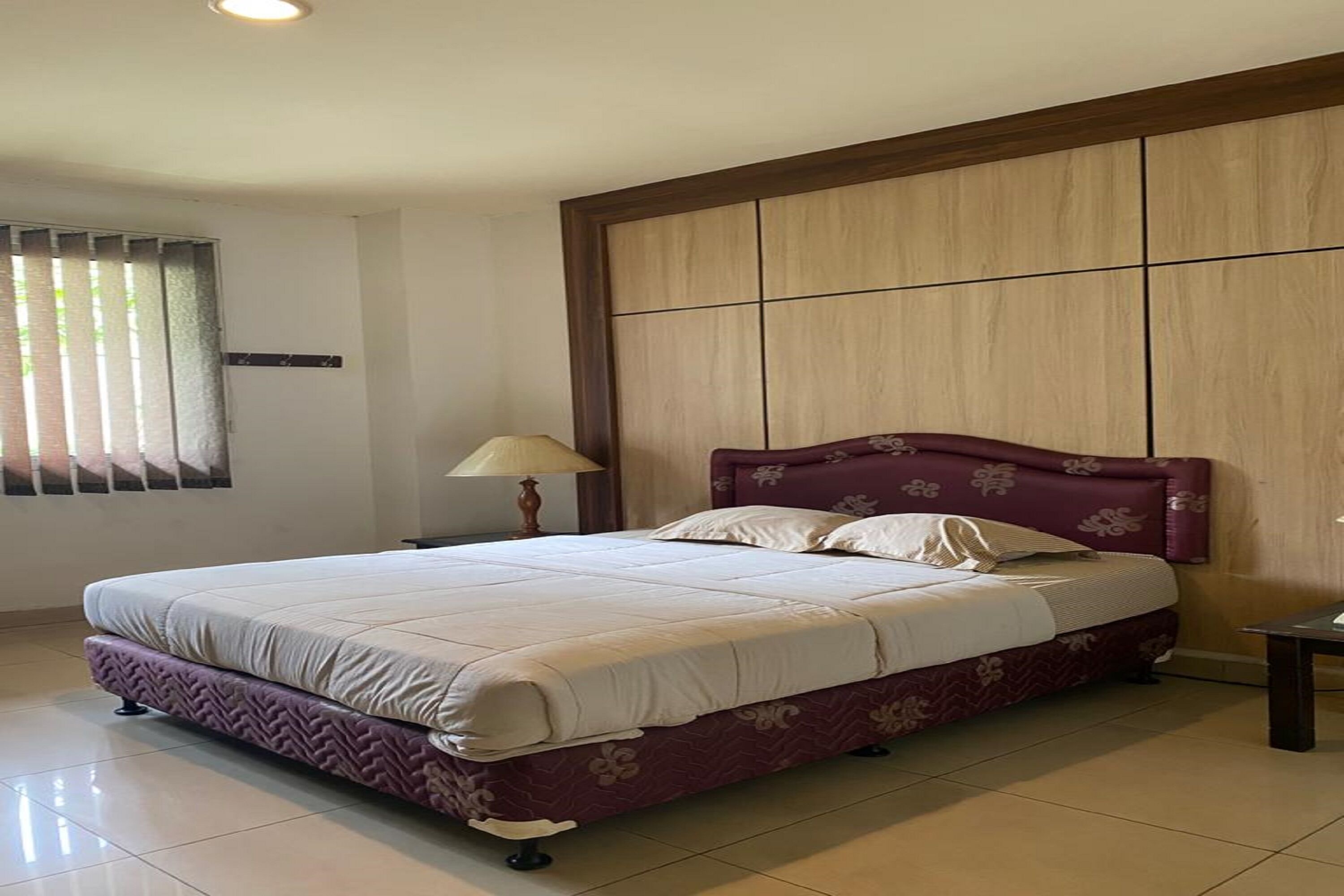 A bedroom with a bed, a nightstand, a lamp, and a window with blinds.