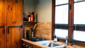 Une cuisine avec des meubles de rangement en bois, un évier à deux bacs et une fenêtre avec des stores.