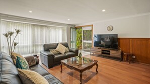A living room with a leather sofa, a glass coffee table, a wooden entertainment unit, and a large TV. - StayAU 4BR Spacious Nature Retreat (Badger Creek)