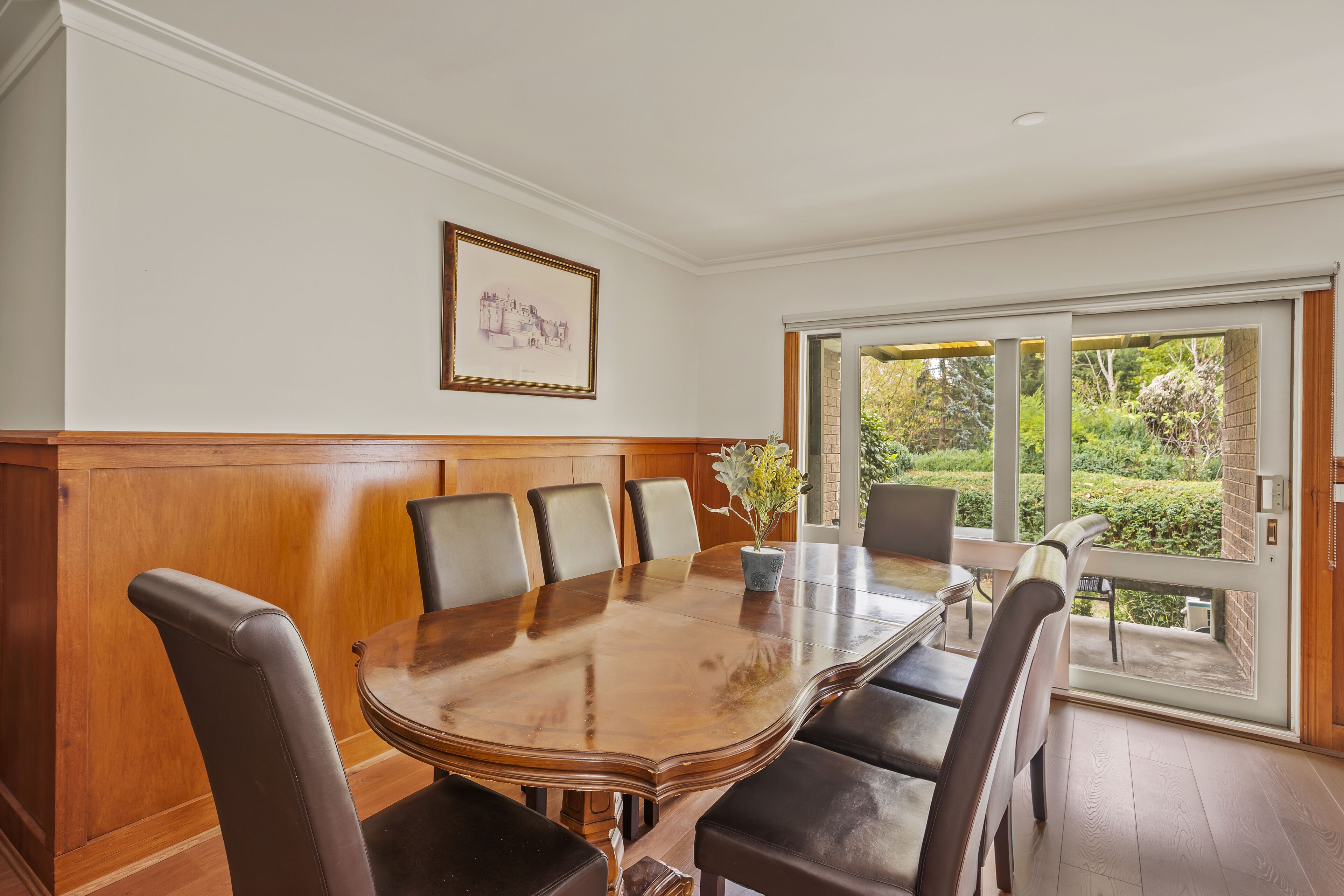 A dining room with a large wooden table, six chairs, and a potted plant.